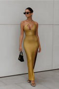 Woman wearing a gold dress with a high slit, standing against a gray wall.